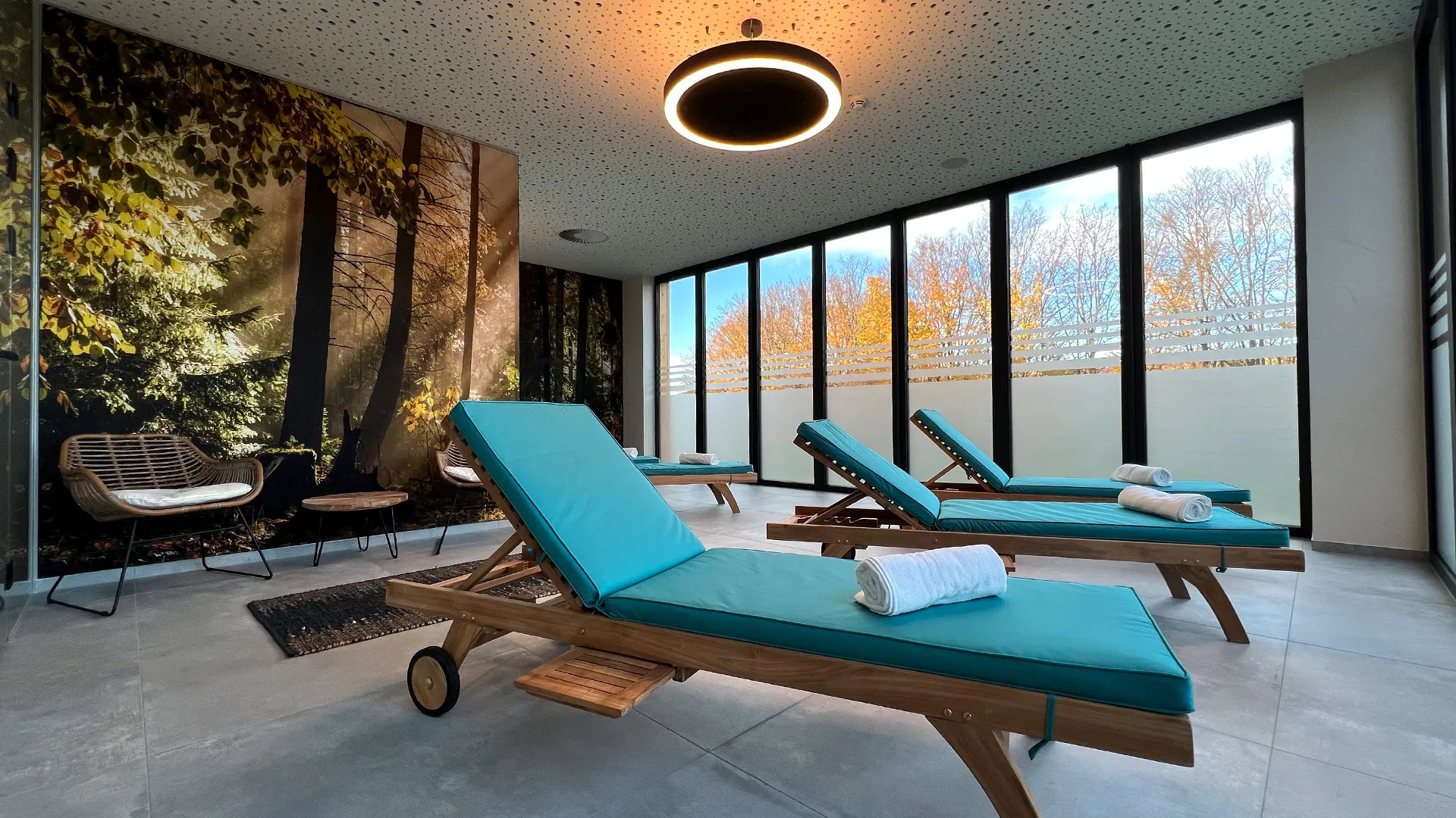 Ein heller, moderner Raum mit großen Fenstern und Wald Tapete mit bequemen Relay Liegen mit Türkise Auflage.