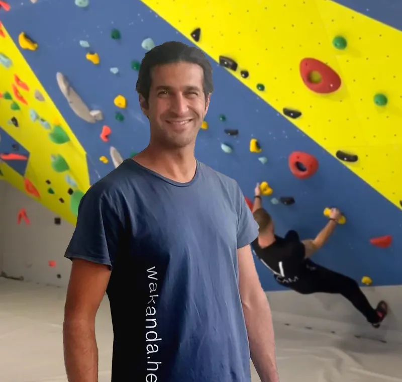 Kletterlehrer steht vor der Boulderwand und lächelt in die Kamera.