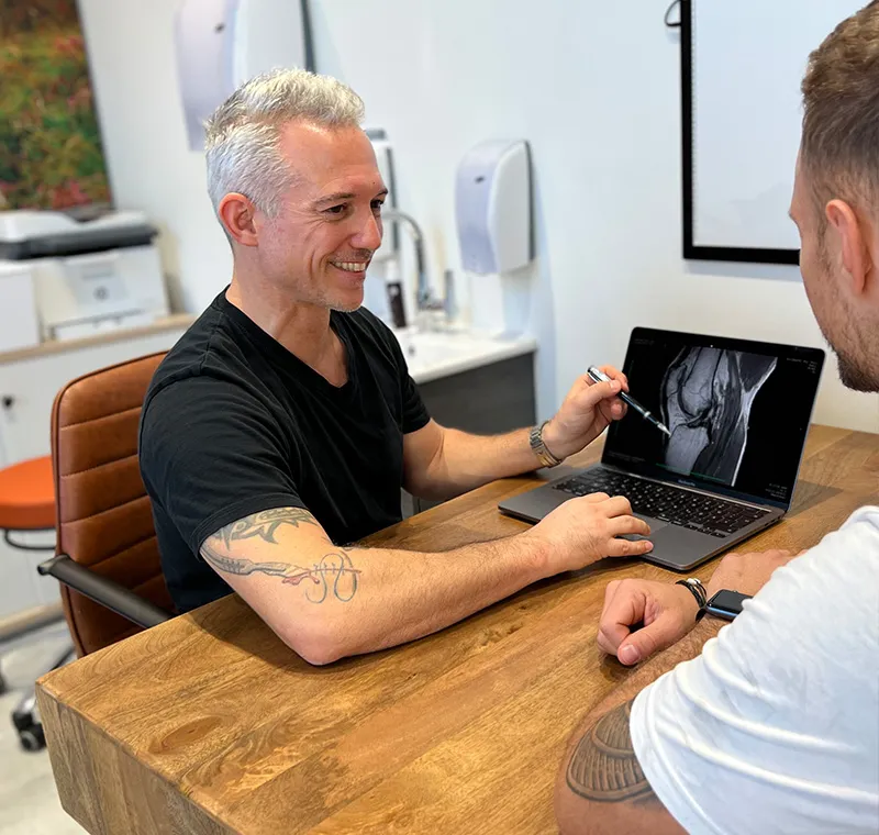Arzt Martin führt ein Beratungsgespräch mit einem Kunden und zeigt ein Röntgen Bild auf dem Laptop.